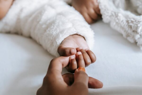crop anonymous black mother holding hand of baby lying on bed